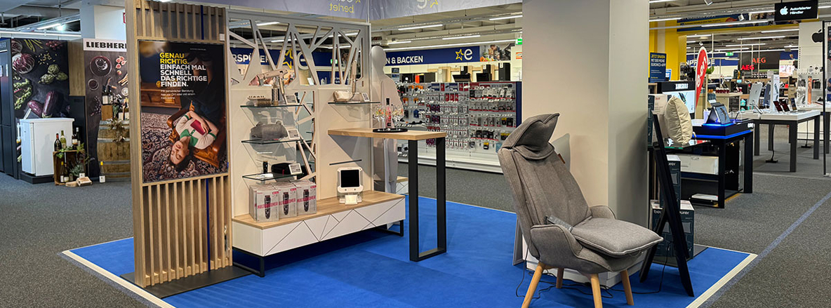 Innenansicht des EURONICS Berlet Marktes mit stilvoller Produktpräsentation, modernen Möbeln und Massagesessel auf blauem Teppich, im Hintergrund Regale mit Elektronikzubehör. Innenansicht des EURONICS Berlet Marktes mit stilvoller Produktpräsentation, modernen Möbeln und Massagesessel auf blauem Teppich, im Hintergrund Regale mit Elektronikzubehör.