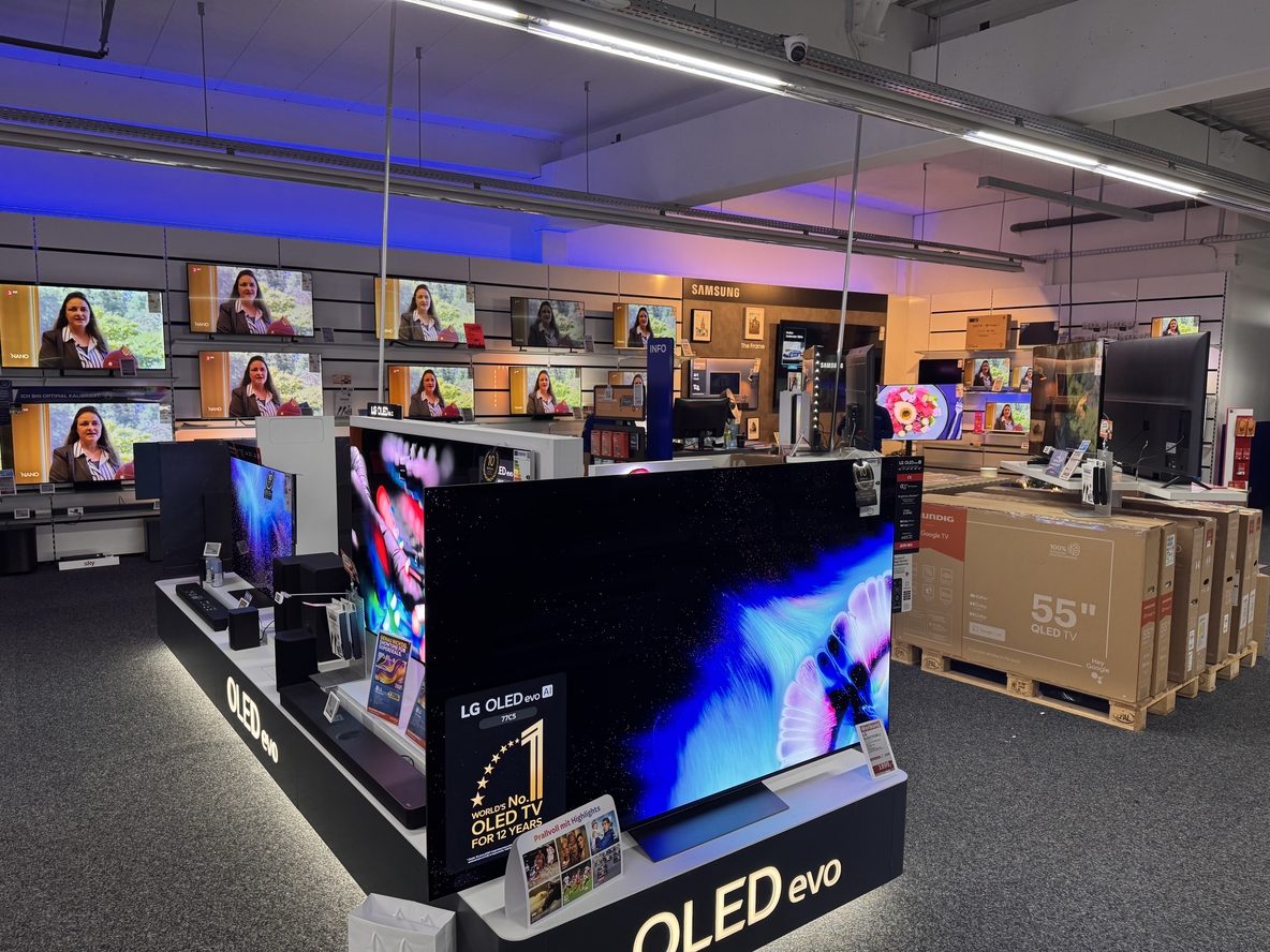 TV-Abteilung bei EURONICS-Berlet-Soest mit großem LG OLED evo Fernseher im Vordergrund, drumherum weitere ausgestellte TVs auf Podesten und an der Wand, sowie gestapelte TV-Kartons auf Paletten im Hintergrund. TV-Abteilung bei EURONICS-Berlet-Soest mit großem LG OLED evo Fernseher im Vordergrund, drumherum weitere ausgestellte TVs auf Podesten und an der Wand, sowie gestapelte TV-Kartons auf Paletten im Hintergrund.