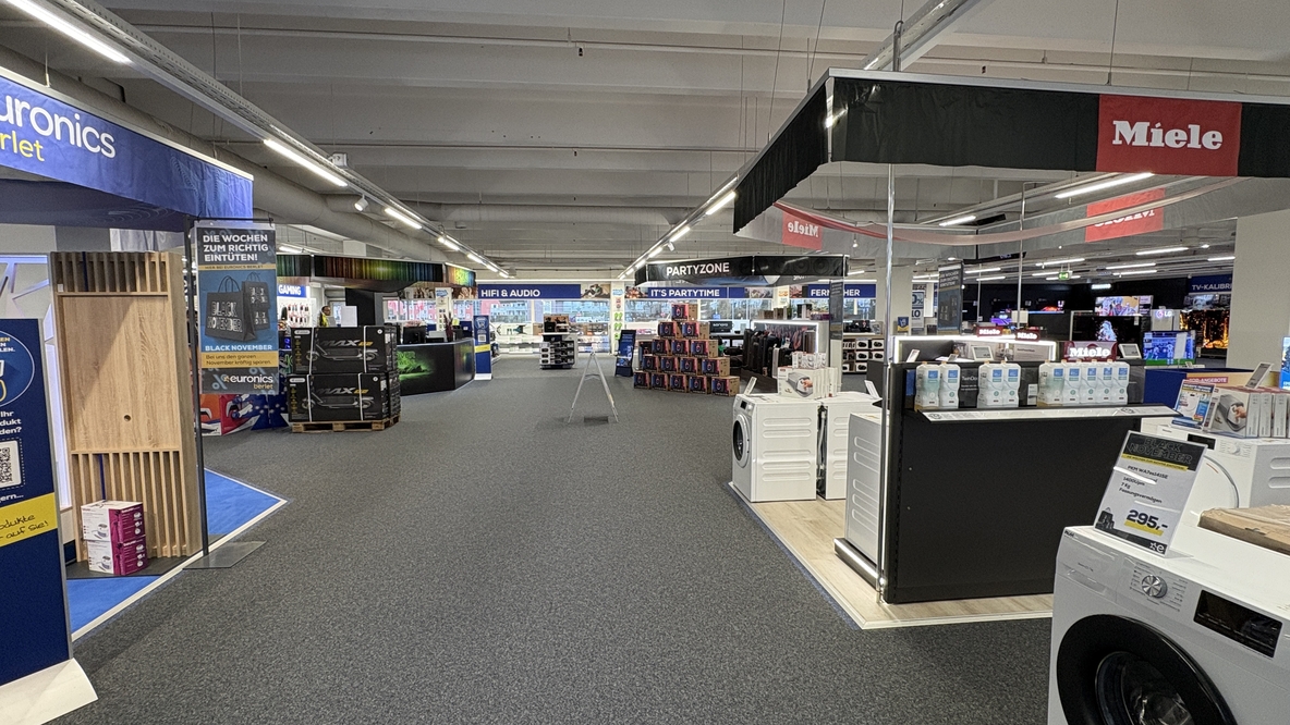 Breite Marktgasse bei EURONICS-Berlet-Unna, mit grauem Teppichboden, links Werbeflächen und Gaming-/HiFi-Bereich, mittig Partyzone mit gestapelten Lautsprechern, rechts Miele-Fläche mit ausgestellten Waschmaschinen und Haushaltsgeräten. Breite Marktgasse bei EURONICS-Berlet-Unna, mit grauem Teppichboden, links Werbeflächen und Gaming-/HiFi-Bereich, mittig Partyzone mit gestapelten Lautsprechern, rechts Miele-Fläche mit ausgestellten Waschmaschinen und Haushaltsgeräten.