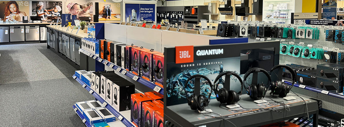 Verkaufsfläche mit Audio-Produkten bei EURONICS Berlet, im Vordergrund JBL-Kopfhörer und Lautsprecher, im Hintergrund Waschmaschinen und Haushaltsgeräte. Verkaufsfläche mit Audio-Produkten bei EURONICS Berlet, im Vordergrund JBL-Kopfhörer und Lautsprecher, im Hintergrund Waschmaschinen und Haushaltsgeräte.