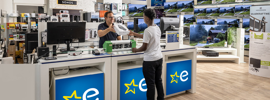 EURONICS Berater spricht mit einem Paar, vor einer TV-Wand.