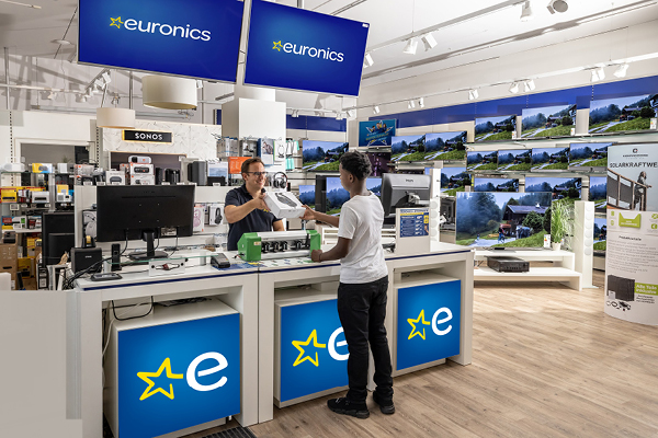 EURONICS Berater spricht mit einem Paar, vor einer TV-Wand.