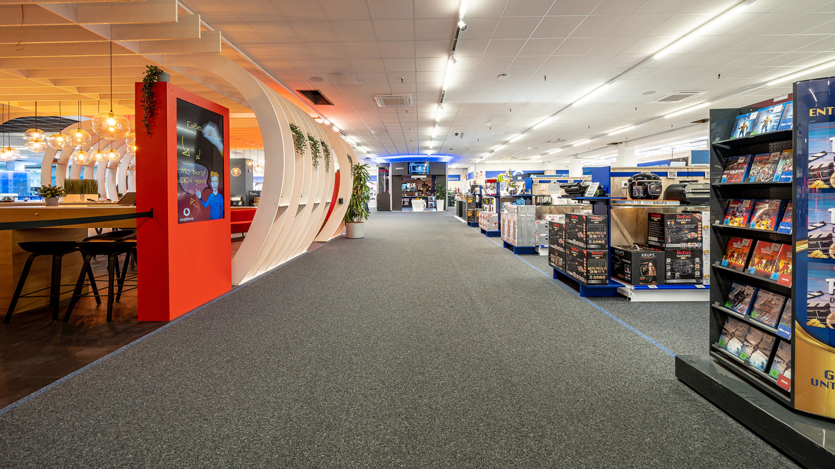 Innenansicht von Euronics Berlet in Hagen mit breitem Gang, Produktregalen rechts und modern gestalteter Sitz- und Beratungszone links von Vodafone