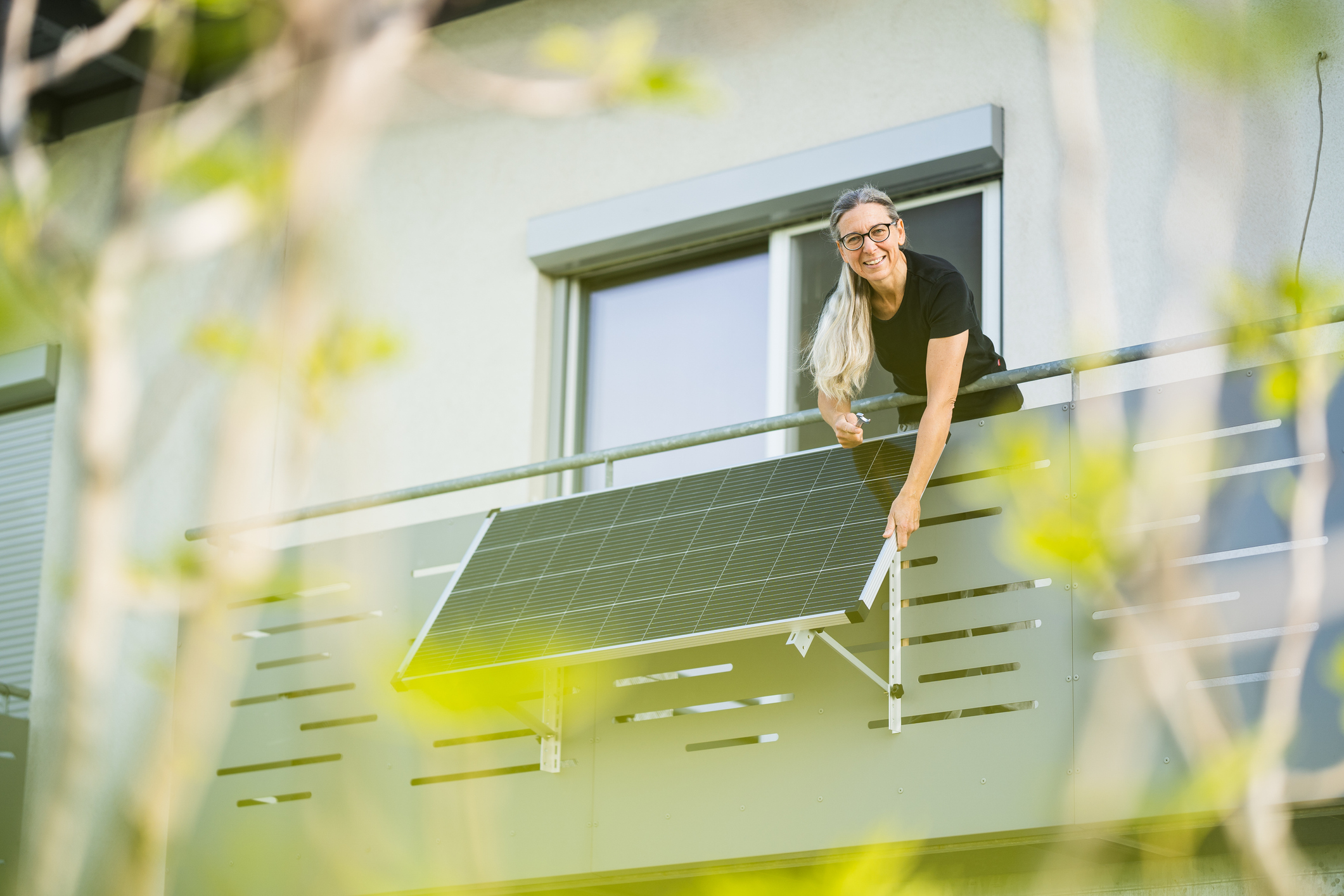 Ältere Frau montiert ein Solarmodul am Balkon