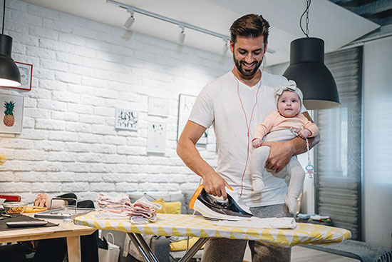 Mann hält Baby und bügelt