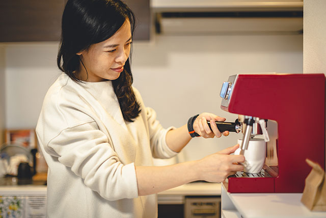 Asiatische Frau macht Kaffee mit einer Siebträgermaschine.