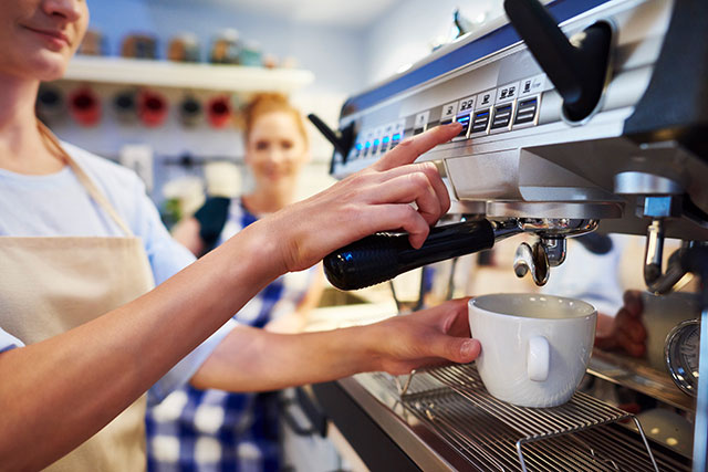 Frau macht Kaffee mit einer Siebträgermaschine.
